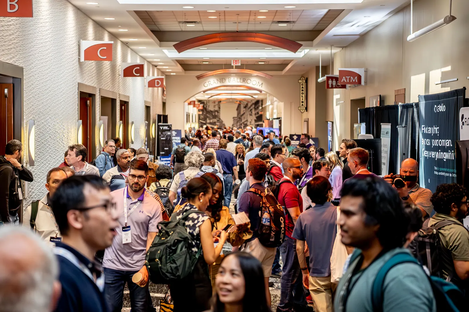 A packed expo corridor at All Things AI 2026, attendees shoulder to shoulder between sponsor tables