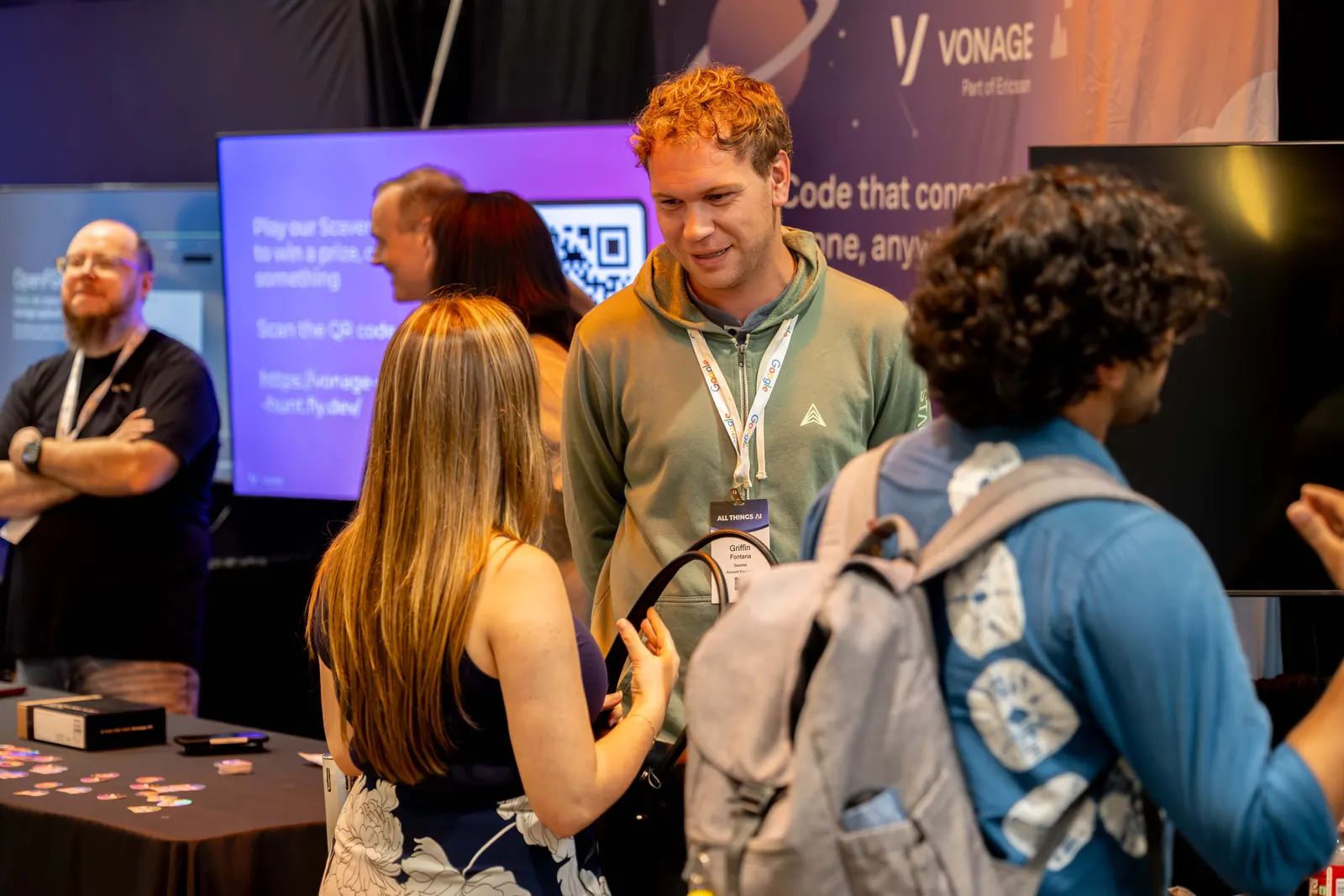 Attendees gathered at the Vonage table at All Things AI 2026, talking with the Vonage team in front of a code demo on screen