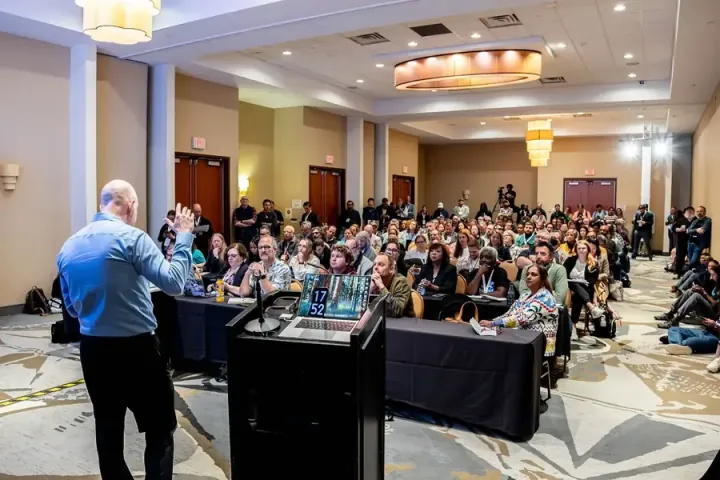 Brent Laster of Tech Skills Transformations teaching a packed breakout room, people sitting on the floor at the front