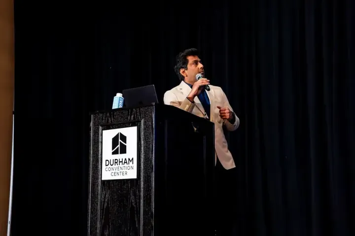 A speaker in a light jacket at the podium against a black stage curtain