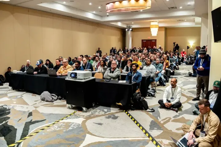 Attendees sitting cross-legged on the floor at the front of a full breakout room, laptops open