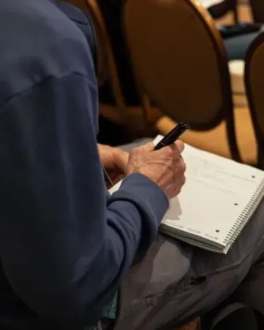 An attendee writing in a spiral notebook on his knee during a session