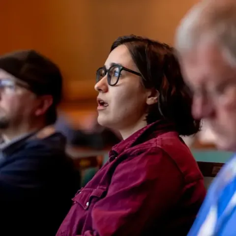 Attendees mid-session, one in glasses asking a question from her seat