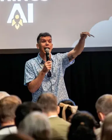 A speaker pointing up at the screen behind him while the front rows look on