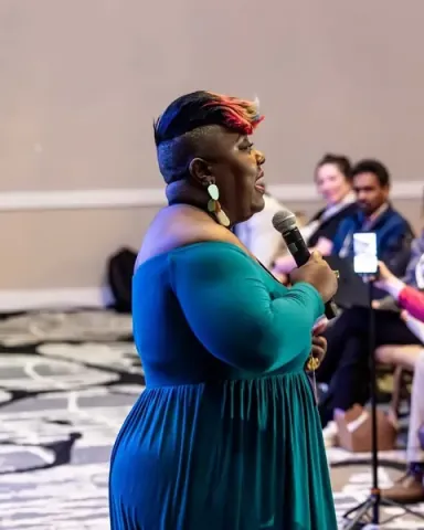 Chisa Pennix-Brown giving an Ignition Talk, walking the aisle with a microphone as the audience turns to follow her