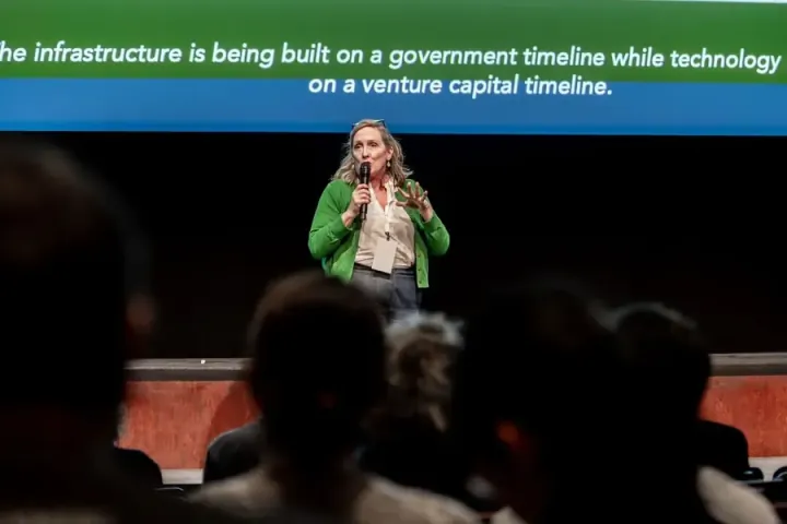 Anjanette Miller, Executive Director of Echo-NC, speaking on the Carolina Theatre stage beneath a slide about infrastructure built on a government timeline