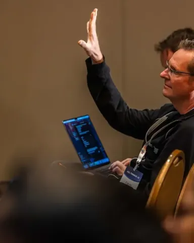 Calvin Hendryx-Parker, CTO of Six Feet Up, raising his hand to ask a question, laptop on his lap