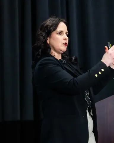A speaker in a black blazer gesturing with both hands as she makes her point