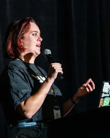 A speaker laughing at the podium, sticker-covered laptop beside her