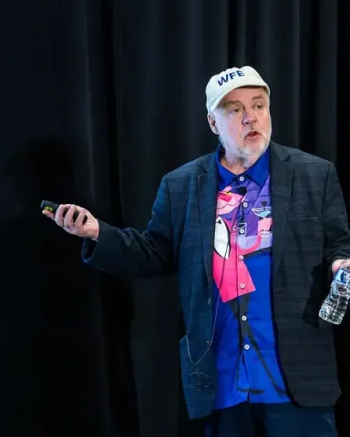 John Willis, a founding father of DevOps and co-author of The DevOps Handbook, speaking on stage with a clicker in hand