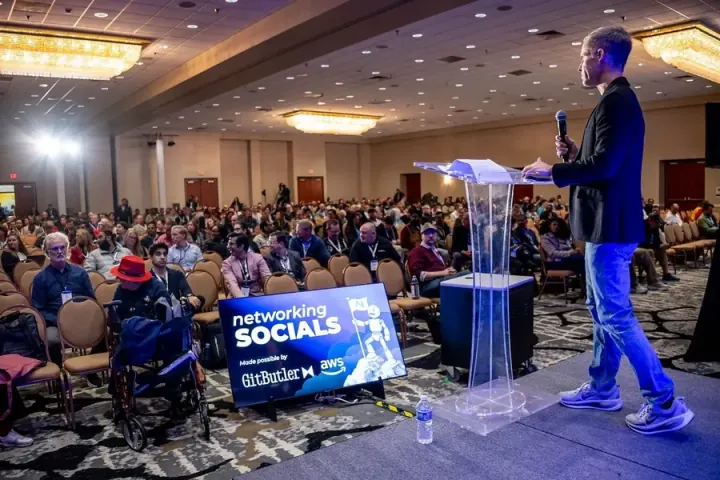All Things AI co-founder Todd Lewis opening the 2026 keynotes from the edge of the stage, a full ballroom in front of him
