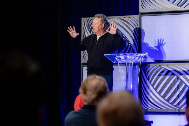 Chris Heivly on the keynote stage with both hands raised, mid-story