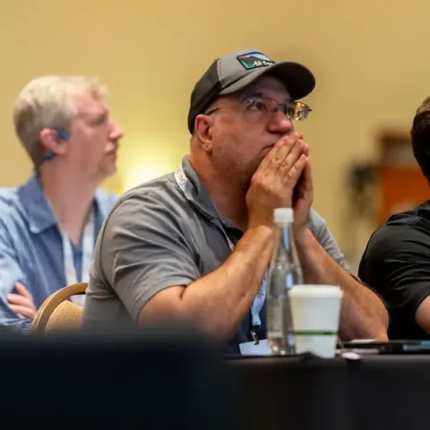 Attendees at a workshop table listening intently, one with his hands pressed together at his face