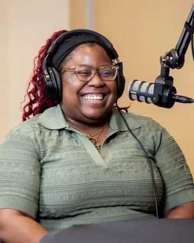 A guest in headphones laughing at the microphone in the podcast booth