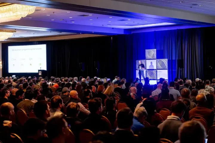A ballroom keynote under blue stage light, the room filled to the back wall