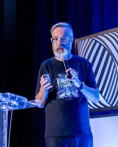 whurley of Strangeworks giving a keynote beside the clear podium, paired on stage with an autonomous agent
