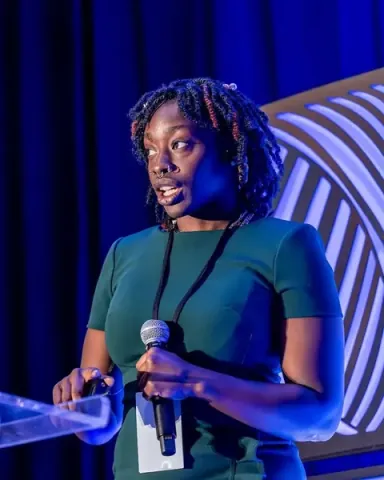 Yassah Reed of Intercom mid-sentence on the keynote stage under blue light, microphone in hand