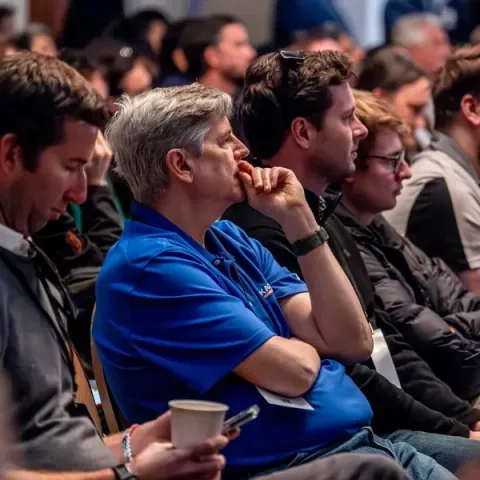 Attendees leaning in during a talk, one with his hand to his chin