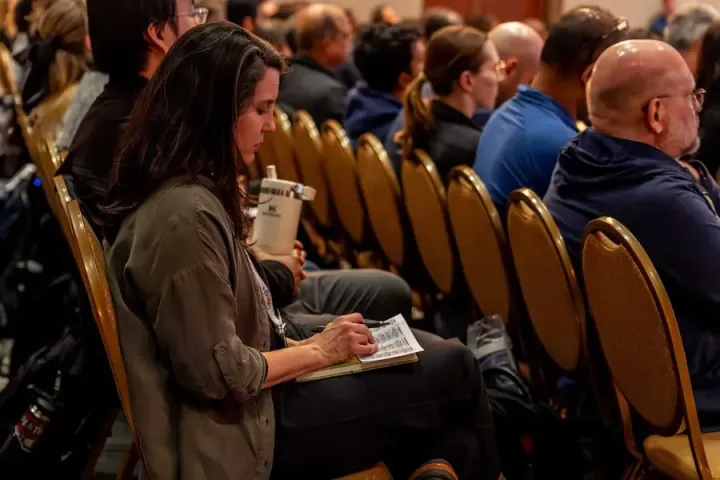 An attendee writing notes on her program in a row of attentive listeners