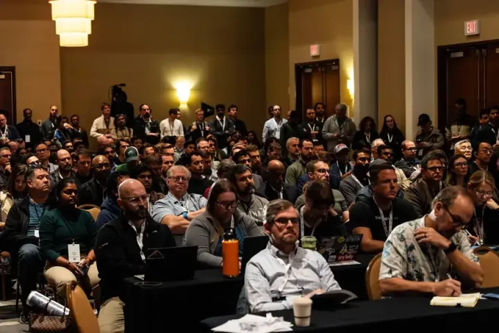 A full breakout room, attendees at tables and in rows taking notes