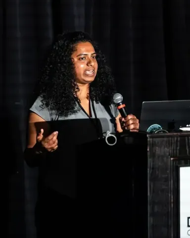 Suha Mokalla, a data scientist at Attention Arc, explaining with her hands at the Durham Convention Center podium