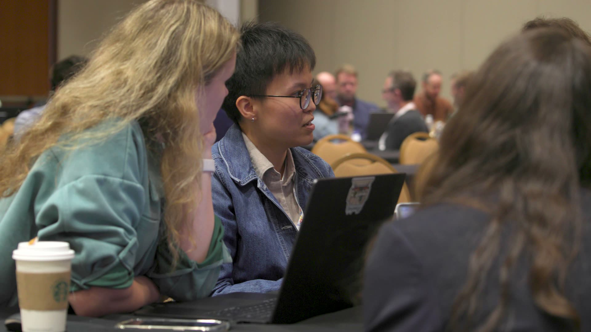 Two people at a workshop table at All Things AI 2026 working through something together on a laptop
