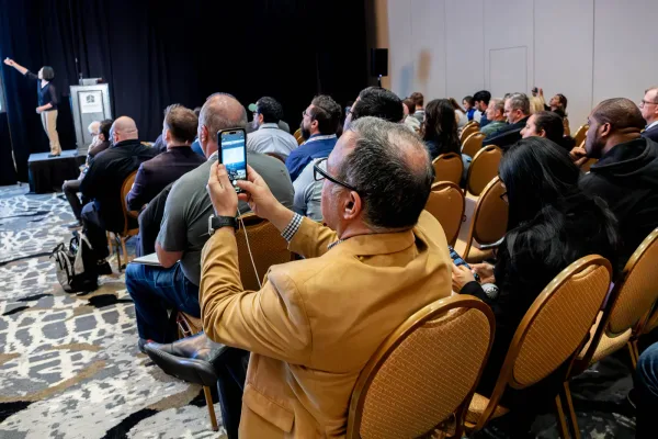 An attendee photographing the presentation while others face the speaker at All Things AI 2026